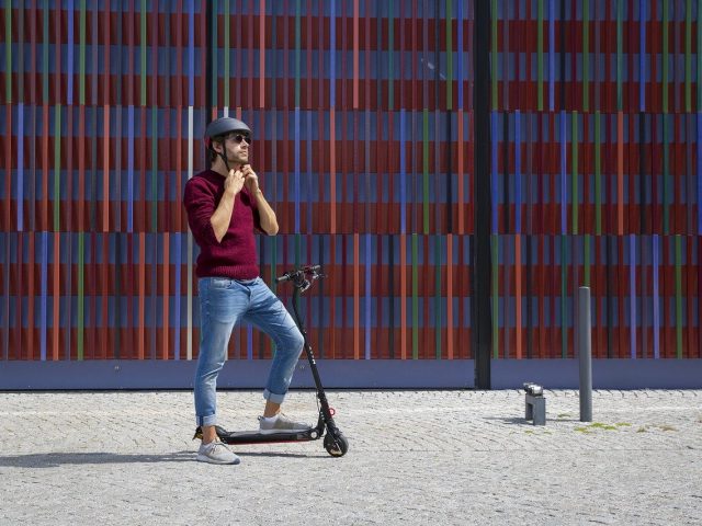 E-scooter with rider adjusting a helmet. Photo credit: https://pixabay.com/photos/e-scooter-munich-urban-city-4921573/