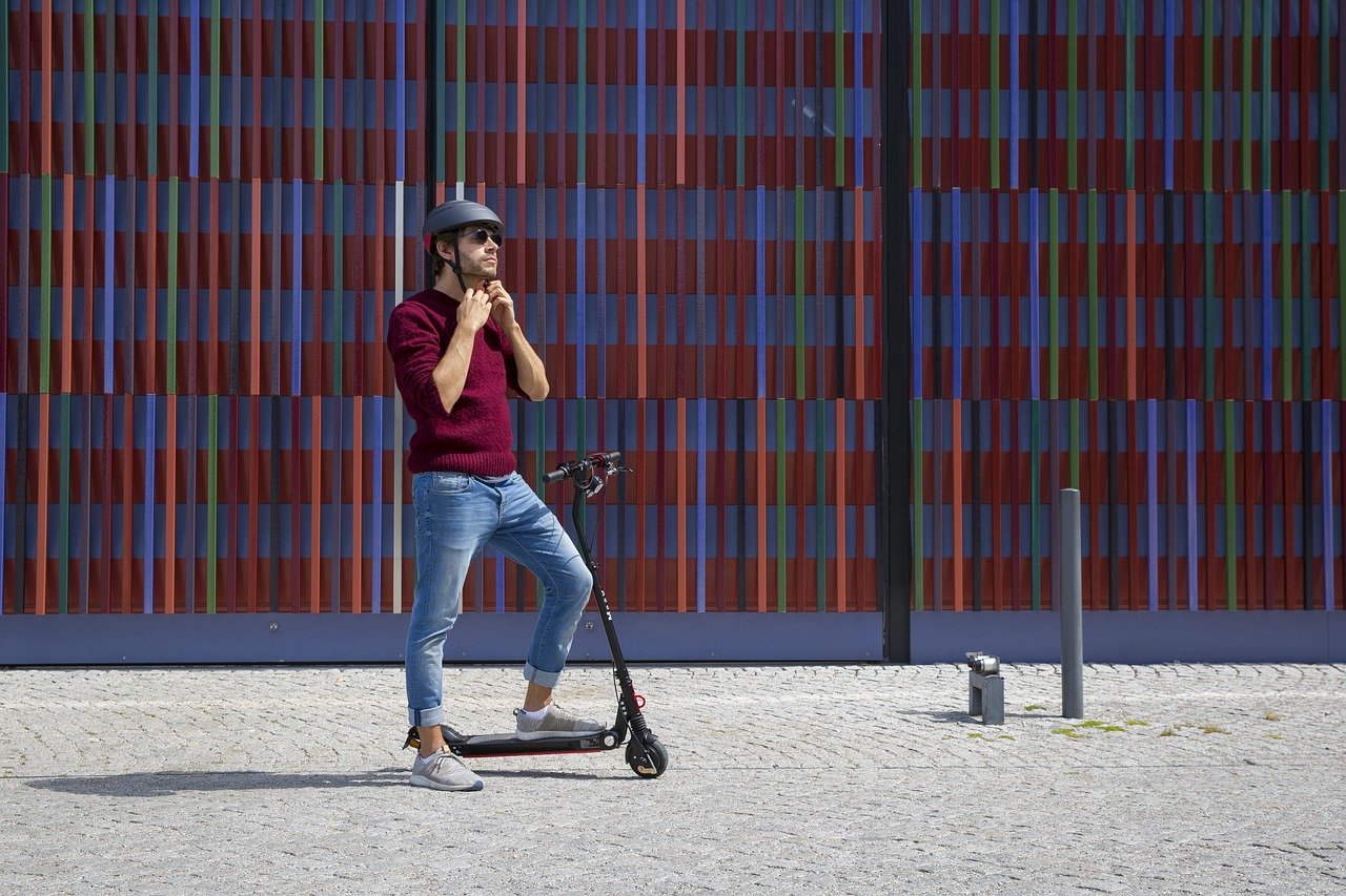 E-scooter with rider adjusting a helmet. Photo credit: https://pixabay.com/photos/e-scooter-munich-urban-city-4921573/